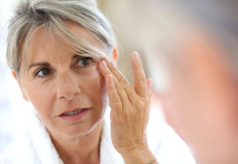 woman looking in the mirror touching her eye after receiving anti-wrinkle injections